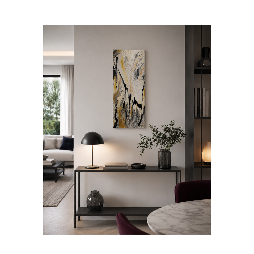 A vertical abstract canvas art print with black, white, and gold brushstrokes, displayed on a light gray wall in a modern, stylishly decorated living room above a console table.