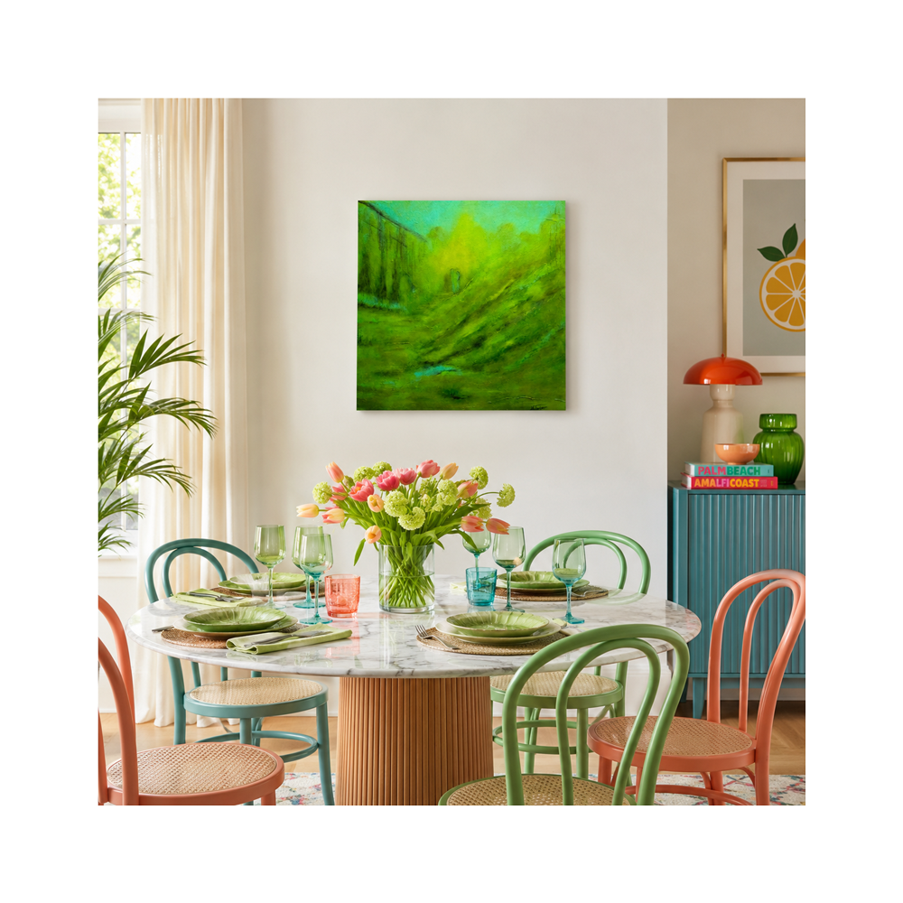 A square canvas wall art print featuring an abstract green landscape hangs on a light gray wall in a styled dining room. The room features a round marble-top dining table with colorful chairs, a floral centerpiece, and other decorative elements.