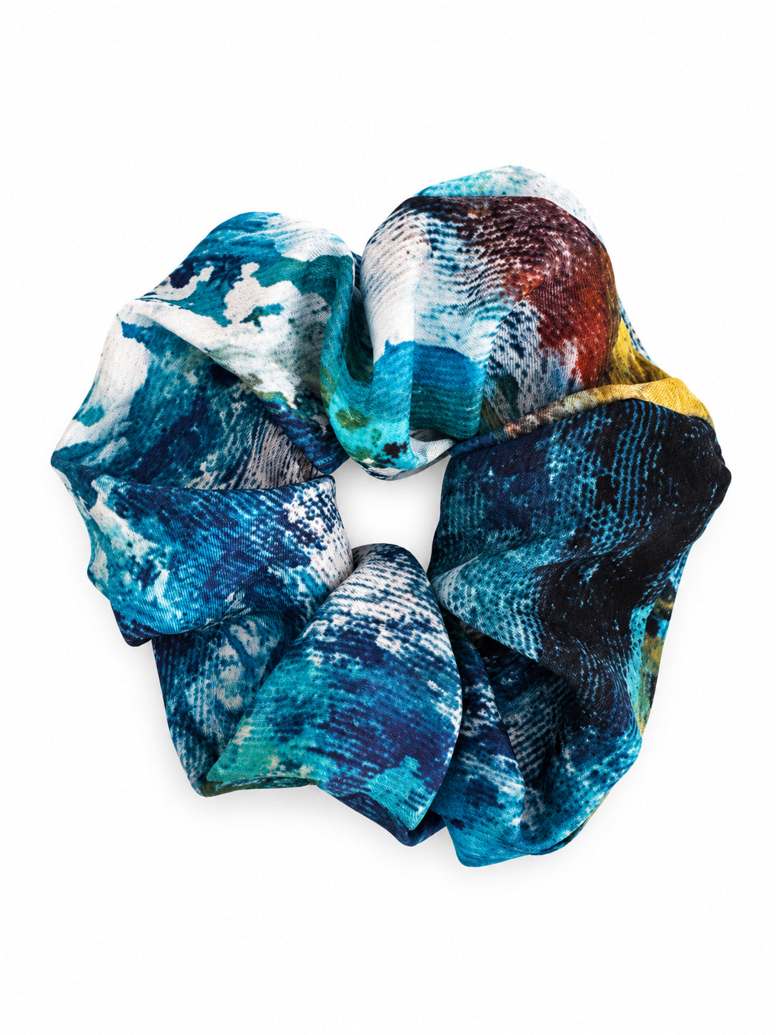 A fabric hair scrunchie featuring an abstract, painterly pattern with shades of blue, teal, white, black, and a touch of yellow, shown on a plain white background.