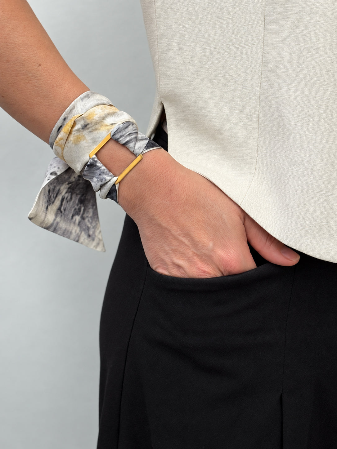 Woman is wearing a white, black and yellow silk scarf at her wrist
