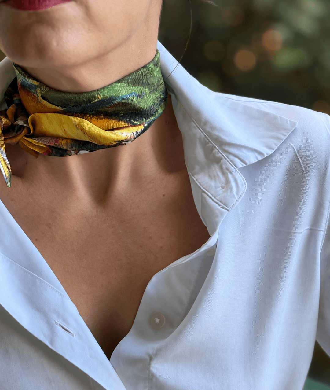 A close-up of a person wearing a white button-up shirt and a patterned silk neck scarf in green, yellow, and black.